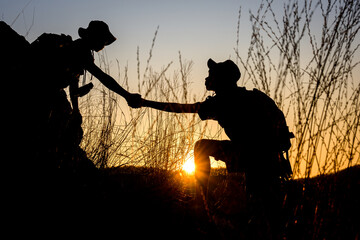Two Boy Scout students showing help to each other Hold hands and pull each other up from the cliff to explore the forest in the evening as the sun sets.