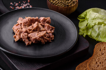 Delicious canned tuna meat on a black ceramic plate on a dark concrete background