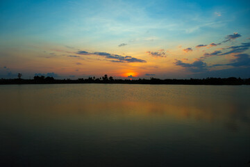 Fototapeta na wymiar beautiful teal and orange color sunset at the lake on agricultural land in the village