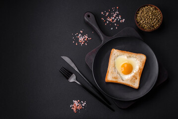 Heart shaped fried egg in bread toast with sesame seeds, flax seeds and pumpkin seeds on a black plate