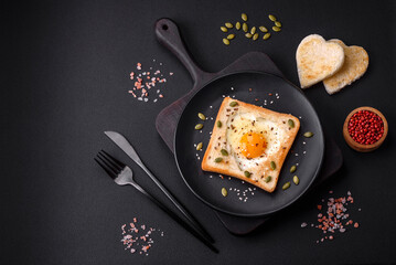 Heart shaped fried egg in bread toast with sesame seeds, flax seeds and pumpkin seeds on a black plate