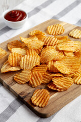 Barbeque Potato Chips on a wooden board, side view. Copy space.