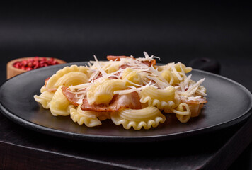 Delicious pasta with bacon and parmesan cheese on a black ceramic plate