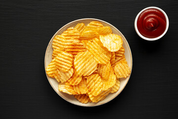Barbeque Potato Chips on a plate on a black background, top view. Flat lay, overhead, from above.