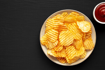 Barbeque Potato Chips on a plate on a black background, top view. Flat lay, overhead, from above....