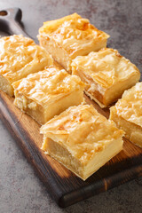 Galaktoboureko is a Greek, Turkish, Laz, and Syrian dessert of semolina custard baked in filo closeup on the wooden board on the table. Vertical