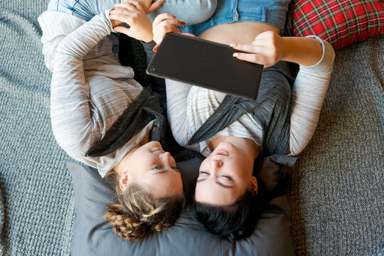 Cheerful caucasian girls sisters lie on floor and watch funny videos on a digital tablet. Happy relationship, at home enjoying the day off