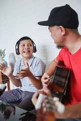 Dad and son singing and playing guitar together while doing video online streaming. Asian family spending quality time at home while recording video on digital camera.