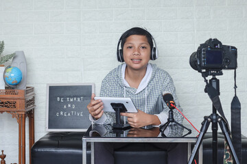 Asian child blogger holding digital tablet while making video blog. Online influencer boy social media live streaming concept.