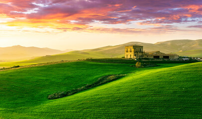 countryside sunset in green hills of spring fields with old castle farm and mountains on background...