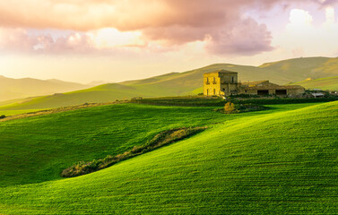 Fototapeta premium sceniv view at a nice farm in green fields in hills and highlands, landscape of spring green hills with mountain bright sunset on backdrop