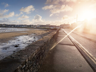 Foot path by Kilkee beach and town houses in the background. County Clare, Ireland. Nobody. Popular summer resort. Atlantic ocean, Irish seascape. Cloudy sunrise sky and sun flare. Calm mood