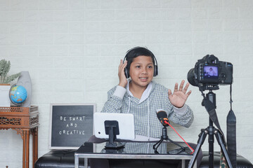 Portrait of confident and creative Asian child blogger talking on camera in a studio making video blog. Online influencer boy social media live steaming concept.