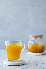 Hot sea ​​buckthorn tea with ginger and honey in a glass cup. Teapot on a terrazzo table. Grey background. Vitamin drink, immune support, cold remedy. Health supplements. Copy space