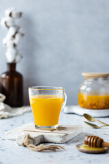 Still life. Table scene with hot sea ​​buckthorn tea with ginger and honey in a glass cup. Grey background. Still life with vitamin drink. Immune support, cold remedy, health supplements. Copy space