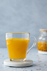 Hot sea ​​buckthorn tea with ginger and honey in a glass cup. Teapot on a terrazzo table. Grey background. Close up. Vitamin drink, immune support, cold remedy. Health supplements. Copy space