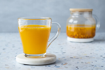 Hot sea ​​buckthorn tea with ginger and honey in a glass cup. Teapot on a terrazzo table. Grey background. Close up. Vitamin drink, immune support, cold remedy. Health supplements