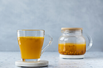 Hot sea ​​buckthorn tea with ginger and honey in a glass cup. Teapot on a terrazzo table. Grey background. Close up. Vitamin drink, immune support, cold remedy. Health supplements. Copy space