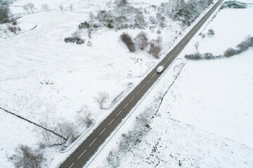 aerial drone view of a vehicle driving on a highway in a snowy landscape