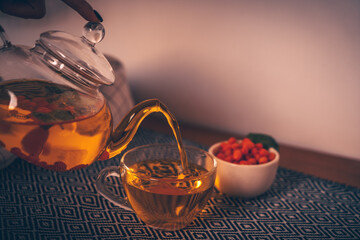 Glass teapot with berry tea on a wooden stand, in a bright kitchen.