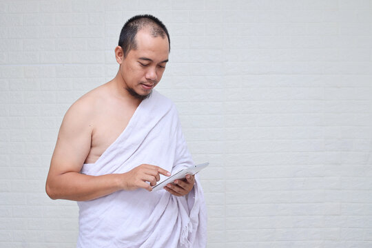 Muslim hajj man wearing white ihram clothes and using digital tablet standing over white background