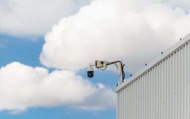 CCD surveillance camera mounted on a hangar in front of a cloudy blue sky. Digital security camera technology concept of surveillance monitoring for property safety.