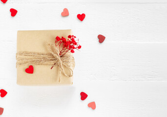  Valentine's Day flatlay. Gift box of craft paper with hearts and red flowers on the white wooden background.