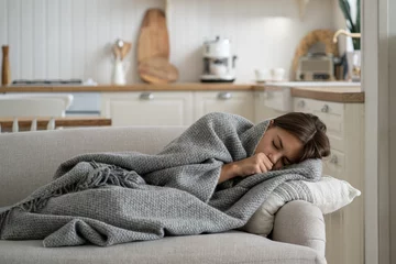 Fotobehang Sick girl child covered with blanket lying on sofa at home coughing, having flu symptoms. Ill kid with fever wrapped with plaid having chills shivering. Children and respiratory viruses © DimaBerlin