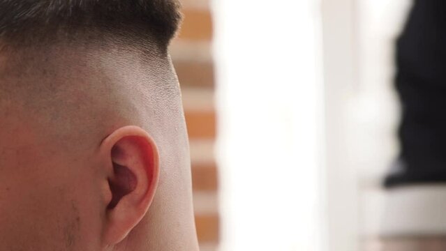 Barbershop. Men haircut in detail. Hands of the master close-up, comb, scissors, shaving machine, stiches. A man sits barber chair. Advertising social networks. Cozy establishment. Men conversations.