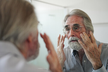old man with gray hair checking hair in front of mirror