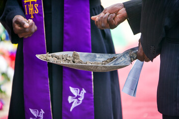 priest and mourner holding a spade with ground to bless the grave - obrazy, fototapety, plakaty