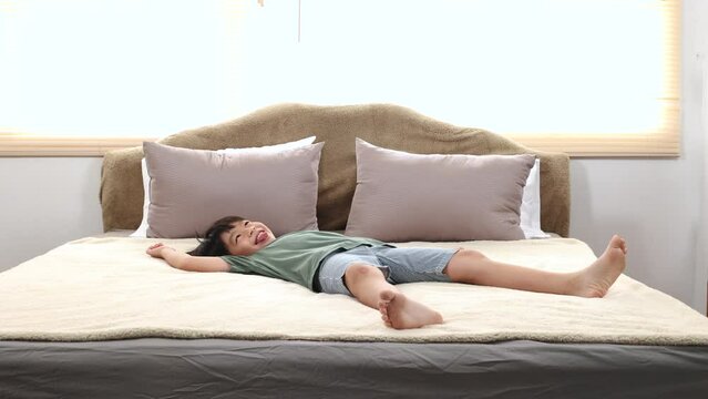 Happy asian elementary school boy jumping on bed and having fun, kid jump on bed switch legs back and forth funny dancing, adorable boy lifestyle happy holiday at home