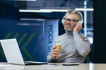 Mature businessman in headphones listening to audio books online podcasts and radio with music, man...