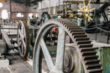 Detail of a gear of a vintage rolling mill. Blurred, old fashioned machines and industrial factory interior in the background.