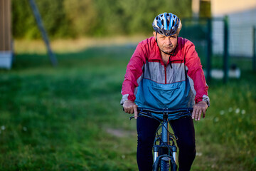 61 year old man rides bike in cycling helmet in countryside with serious face. © grigvovan