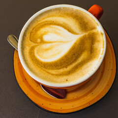 Cup of coffee with a heart pattern made of milk in a brown cup from above