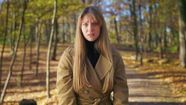 Front view of angry, young lady standing in park, looking at camera. Beautiful, elegant woman walking in park, wearing fashionable clothes, showing no. Concept of sincere emotions.