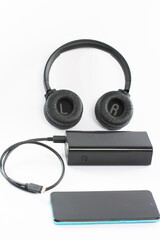 Wireless bluetooth headphones on white background with power bank and charging cable and phone.