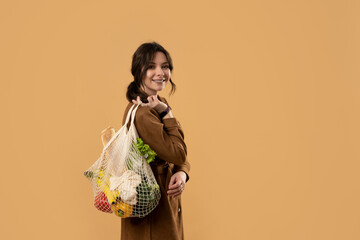 Young brunette woman holding reusable cotton shopping mesh bag with organic groceries from a market. Concept of no plastic. Zero waste, plastic free. Sustainable lifestyle.