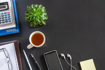 Black office desk with notebook, calculator, diary and smartphone with headphones. Top view with...