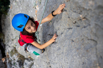 child rock climber in a blue protective helmet overcomes the route in the mountains. children's...