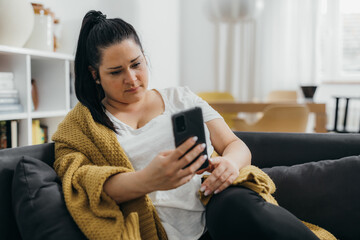 young adult woman relaxing on sofa at home using mobile phone