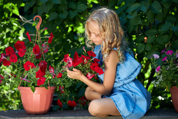 caucasian young blonde girl in a blue dress takes care of flowers in the garden