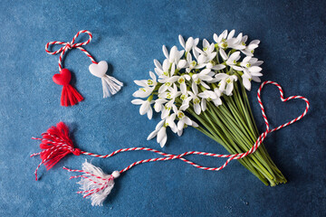 A bouquet of snowdrops flowers and a red and white rope with tassels, a symbol of the arrival of spring on a blue background. Postcard for the feast of March 1 Martisor and Baba Marta - 567658717