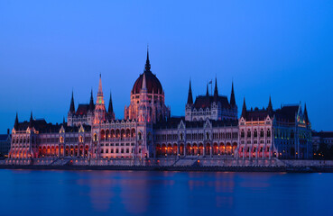 Fototapeta na wymiar The Hungarian Parliament in Neo-Gothic style from across the Danube at blue hour. long exposure. blue sky. travel destination. Famous and popular Budapest landmark and tourist attraction. City skyline