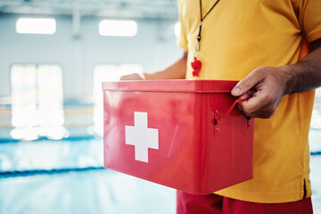 Box, safety or hands of a lifeguard by a swimming pool helping rescue the public from water danger or drowning. Zoom, trust or man with a medical kit ready for emergency injury support in an accident