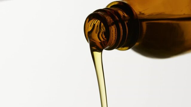 Side view macro shot of almond oil is being poured from brown reagent bottle on grey background | Abstract face care cosmetics ingredients formulating concept