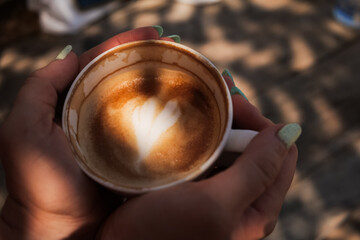 Woman hands holding cup of cappuccino coffee with heart shape. 