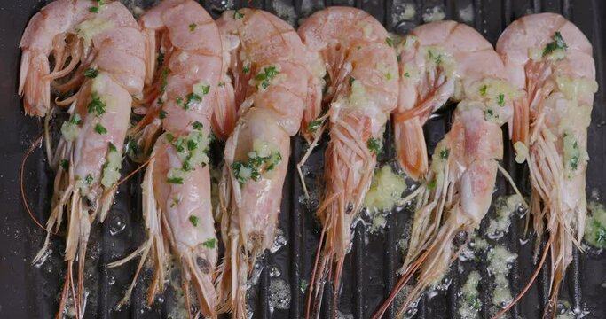 Straight down view of a row of beautiful pink shrimp frying in a pan with garlic butter, parsley and olive oil
