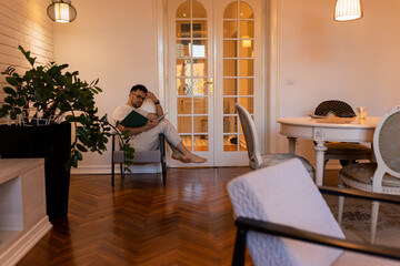 A man sitting in the chair and reading a book alone in the apartment